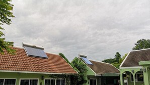 Una hilera de edificios verdes con techos de tejas y paneles solares, un coche estacionado al frente y un camino de entrada pavimentado.