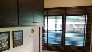 Una cocina con armarios de madera oscura, una encimera blanca, una ventana con persianas y un cubo de basura.