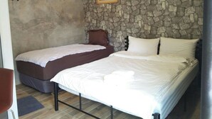 Un dormitorio con pared de piedra, dos camas, una silla y un equipo de aire acondicionado.