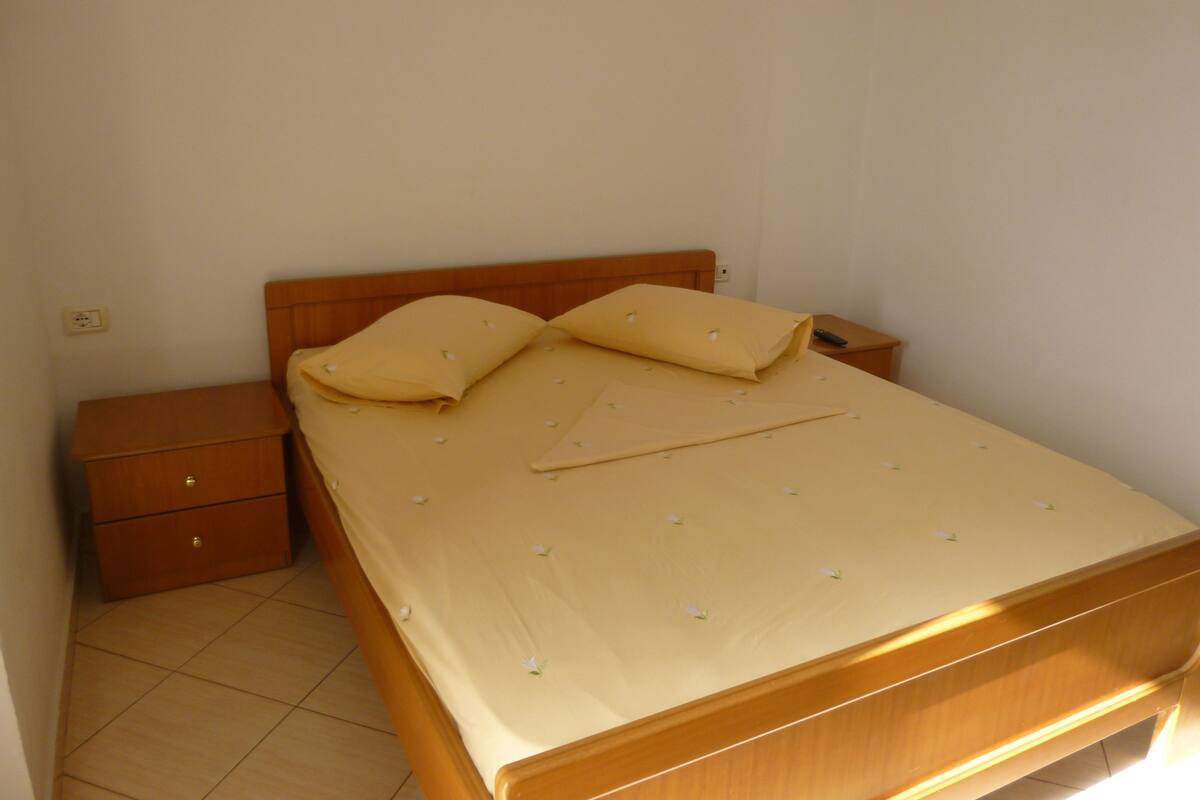 A single bed with a wooden headboard, a nightstand with a drawer, and a small bedside table with a remote control.