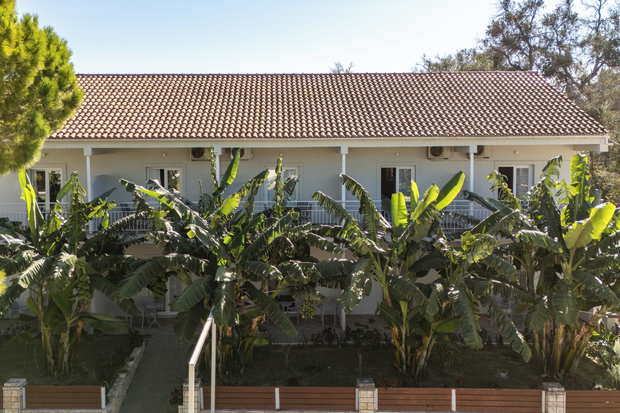 A two-story building with a tiled roof, surrounded by banana plants.