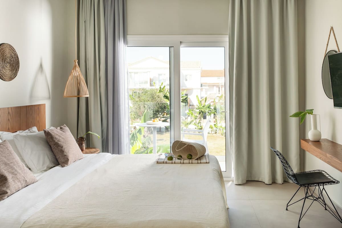 Un dormitorio con una cama grande, una mesita de noche con lámpara, una silla y vistas al exterior.