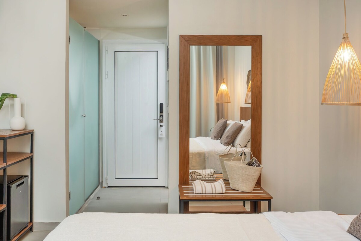 Habitación de hotel con una cama, una mesita de noche con lámpara, un espejo y una puerta.