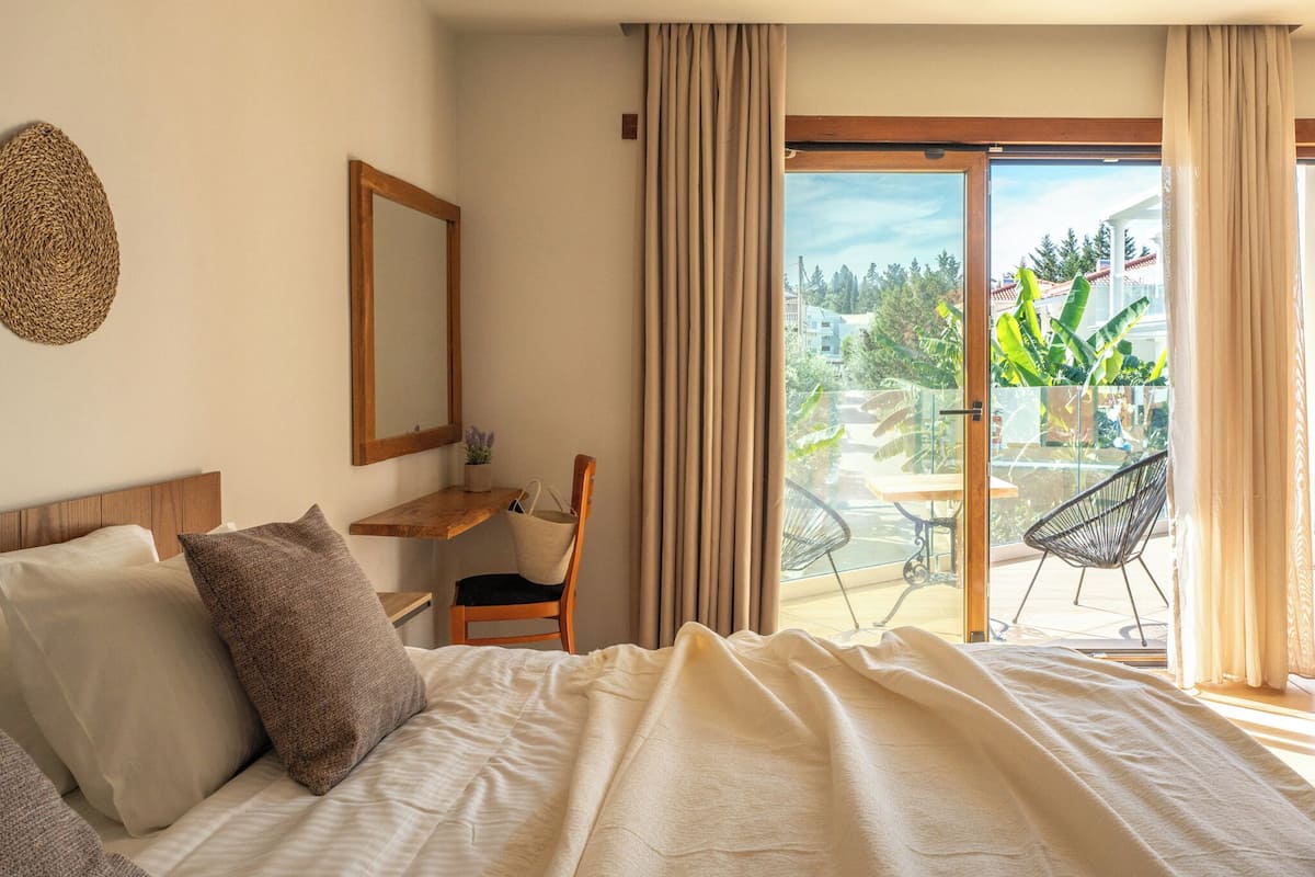 Un dormitorio con cama, una mesita de noche de madera, una silla y vistas al exterior a través de una puerta corrediza de vidrio.