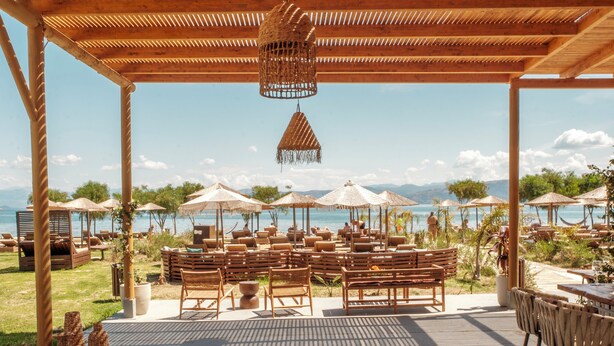 Un área de estar al aire libre con muebles de madera y sombrillas, con vista a una masa de agua.