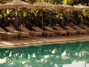 Zona de piscina con sillas de descanso y sombrillas.
