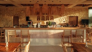 Zona de bar con muebles de mimbre, paredes de piedra y lámparas colgantes.