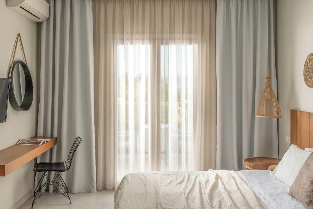 Un dormitorio con cama, escritorio, silla y ventana con cortinas.