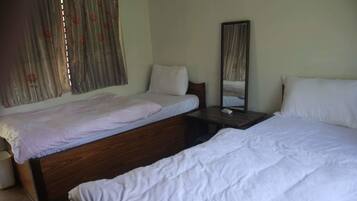 A bedroom with two single beds, a wooden headboard, a bedside table with a mirror, and a window with curtains.