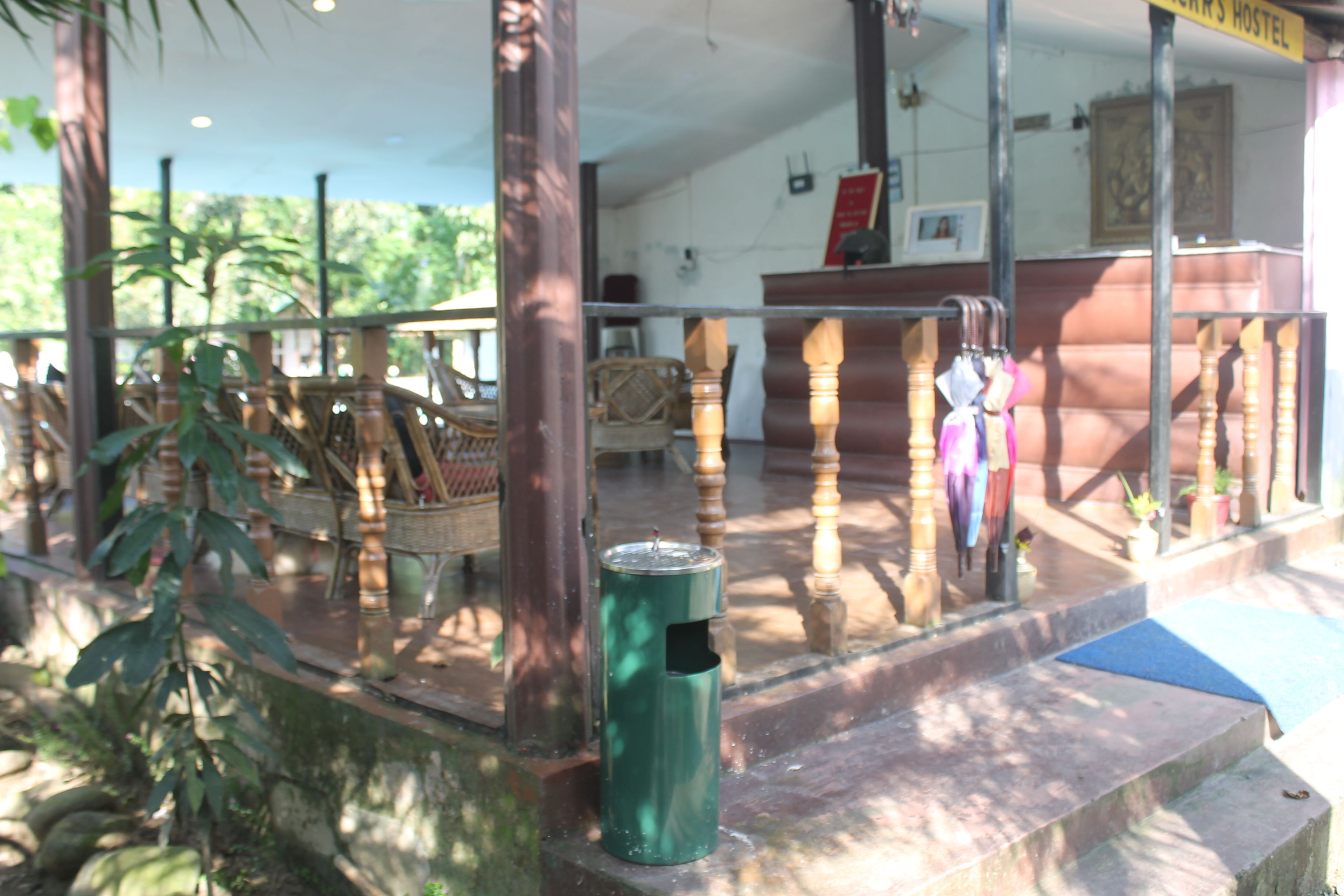 Un espace extérieur abrité comprenant une poubelle verte, des chaises en bois et un escalier menant à un niveau supérieur.