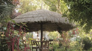 A thatched-roof outdoor seating area with wooden chairs and a table, surrounded by lush greenery.