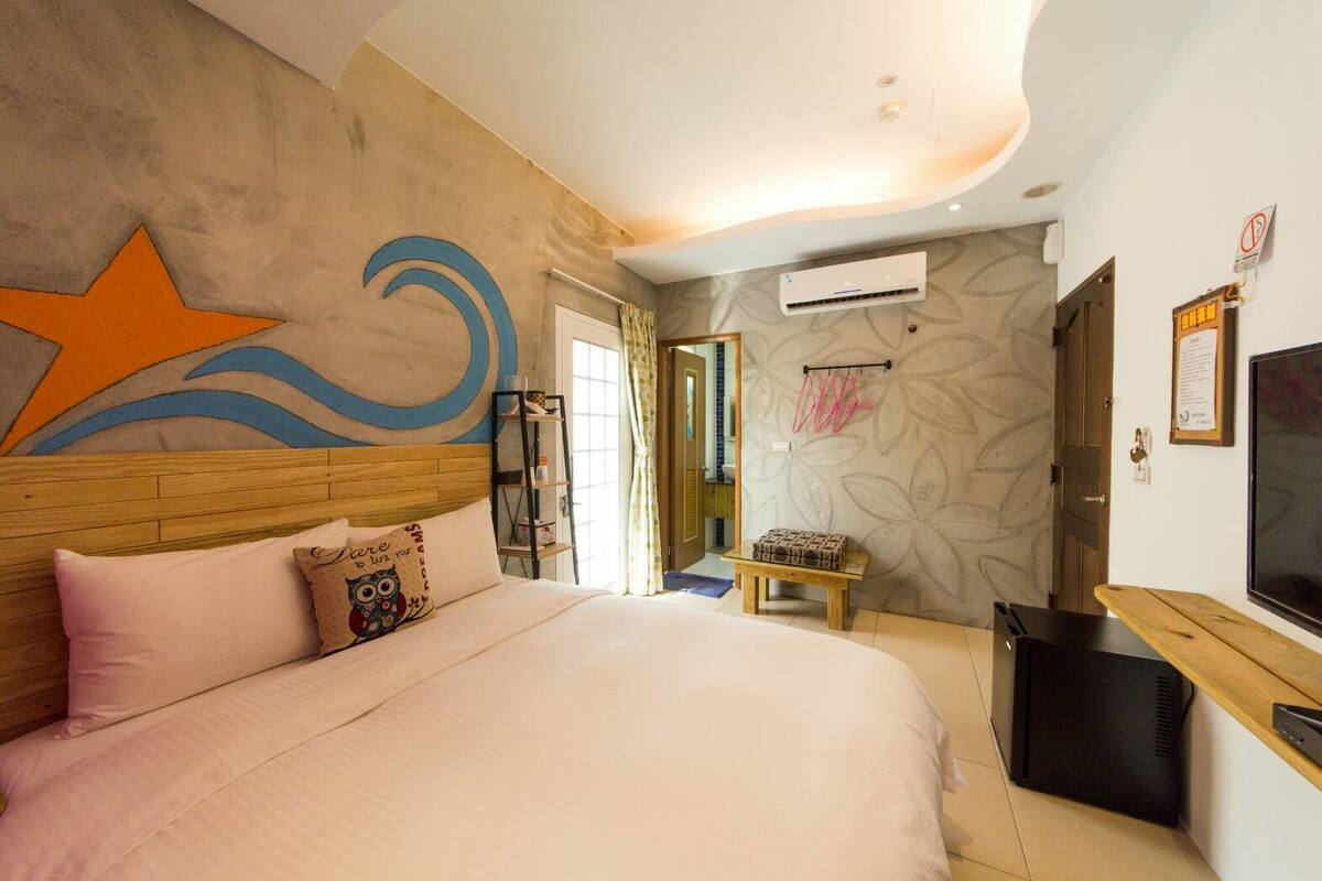 A bedroom with a large bed, a TV, a wooden headboard, and a wall with a decorative design.