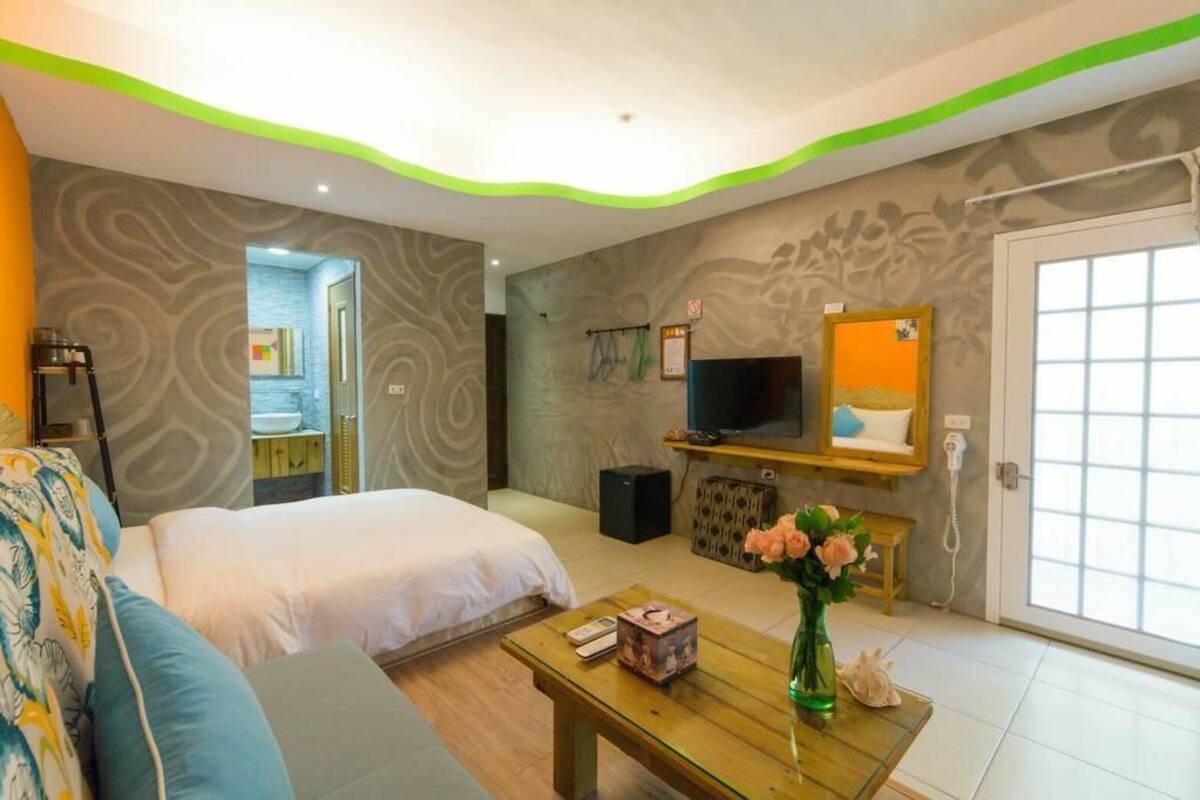 A hotel room with two beds, a television, a small table with a vase of flowers, and a bathroom visible through an open door.
