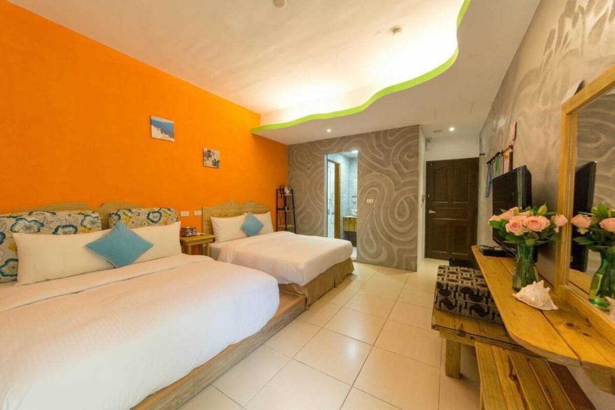 A hotel room with two beds, a wooden bench, a mirror, and a vase of flowers.