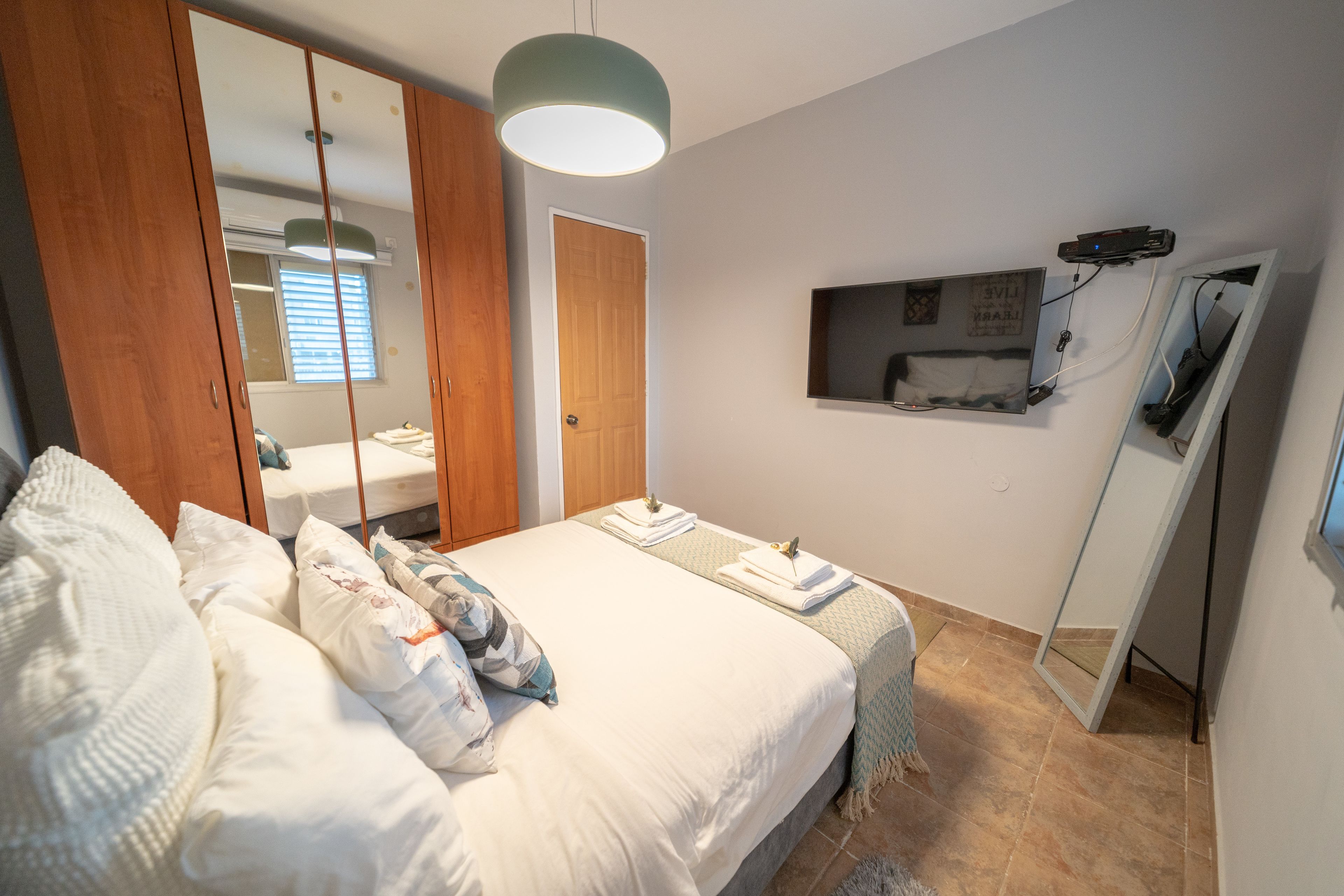 A bedroom with a bed, a wardrobe, a mirror, a television, and a ceiling light.
