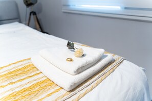 A neatly made bed with a white and yellow striped blanket, a folded white towel, and a decorative item on the bed. - YalaRent Shaldag 2BR APT - Families only (Eilat)