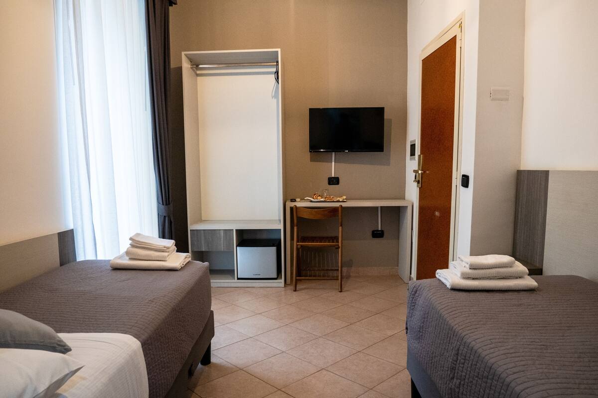 Une chambre d’hôtel avec deux lits, un bureau, une télévision et une petite poubelle.