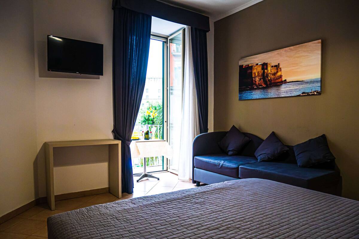 Une chambre d’hôtel avec un lit, un bureau, un canapé, une télévision et un tableau.