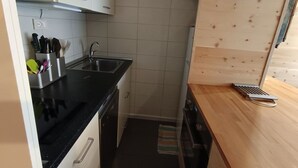 Cozinha compacta com bancada preta, pia de aço inoxidável e armários de madeira.