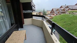 Uma varanda com um banco de madeira, vista para uma colina verde e edifícios tradicionais em estilo chalé ao fundo.
