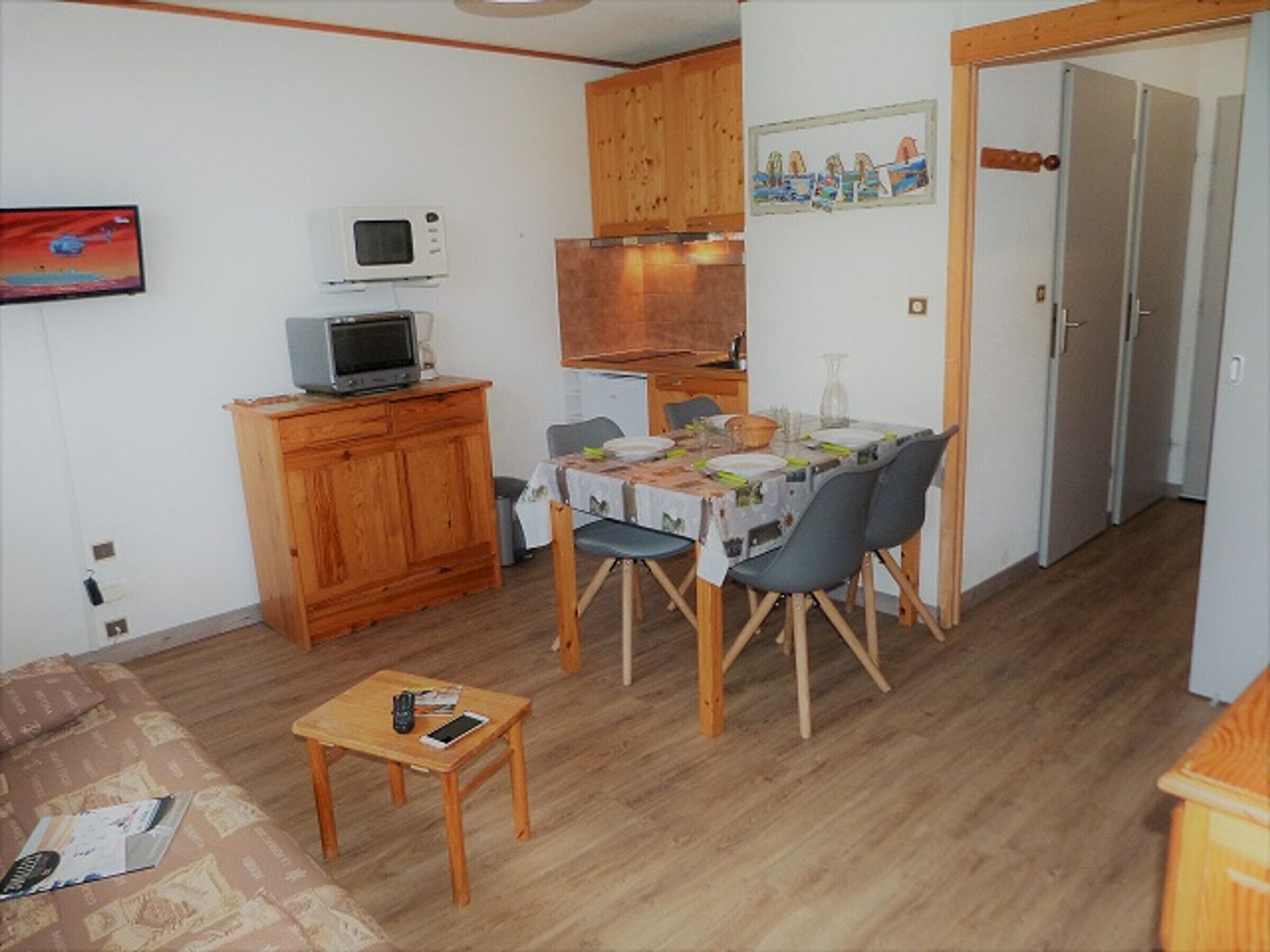 A compact living space with a dining table, chairs, a small TV on a cabinet, and a door leading to another room.
