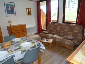 Una habitación amoblada con una mesa de comedor para dos personas, un sofá, un aparador de madera y una ventana con cortinas.