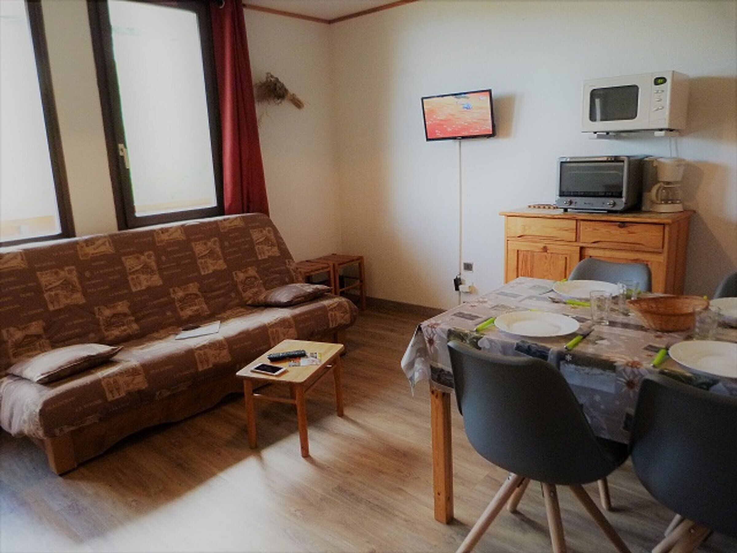 Un salon comprenant un canapé, une petite table, un téléviseur, un four à micro-ondes et un coin repas avec des chaises et une table dressée pour deux personnes.