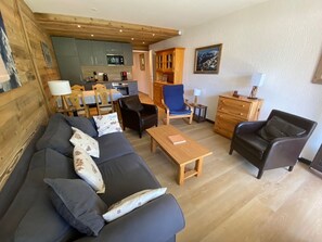 A cozy living room with a sofa, chairs, a coffee table, and a kitchen in the background.