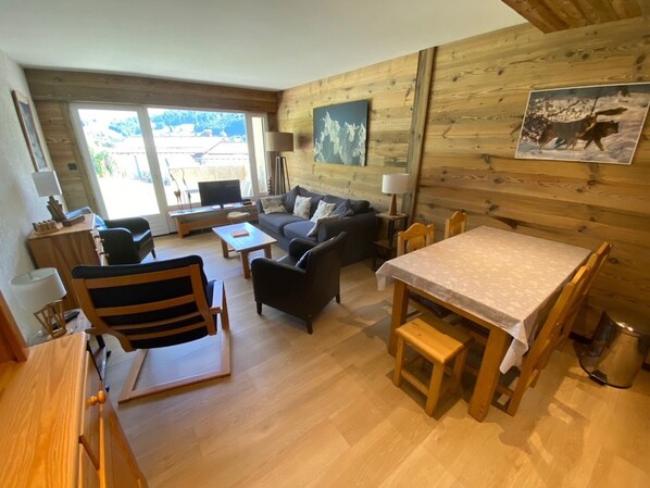 A cozy cabin interior with a wooden interior, a sofa, a dining table, and a TV.