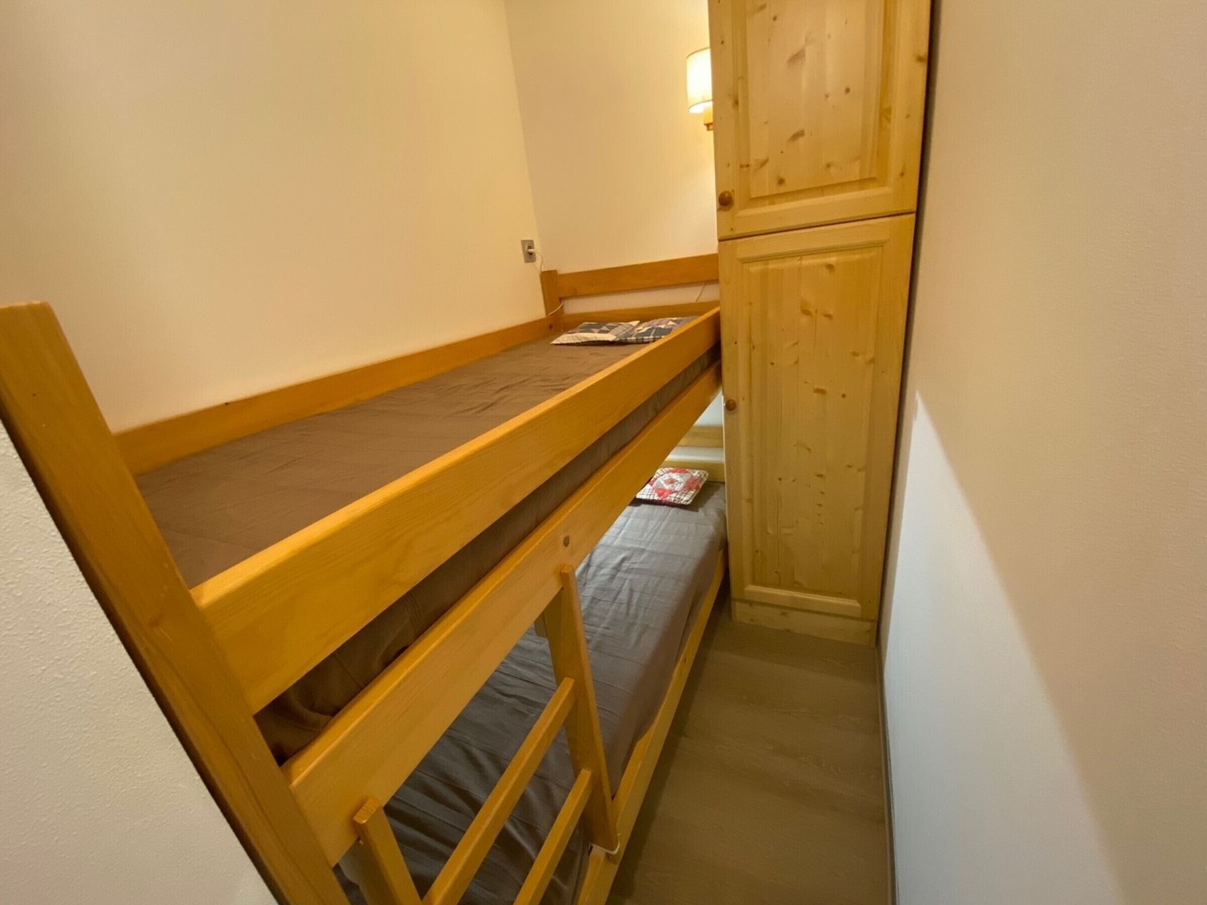 A narrow room with a bunk bed and a wooden cabinet.