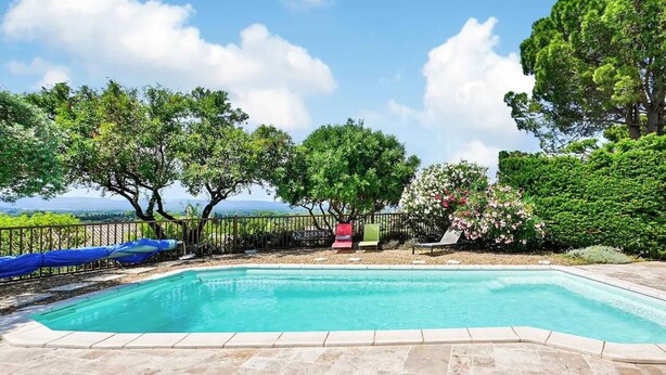 Una piscina con solárium alicatado, rodeada de árboles y una valla.