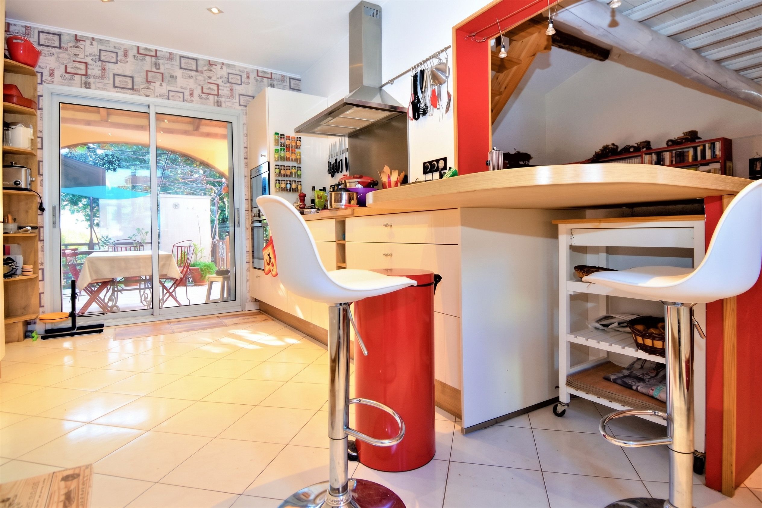 A modern kitchen with a central island, bar stools, and a view of the outdoors through a glass door.