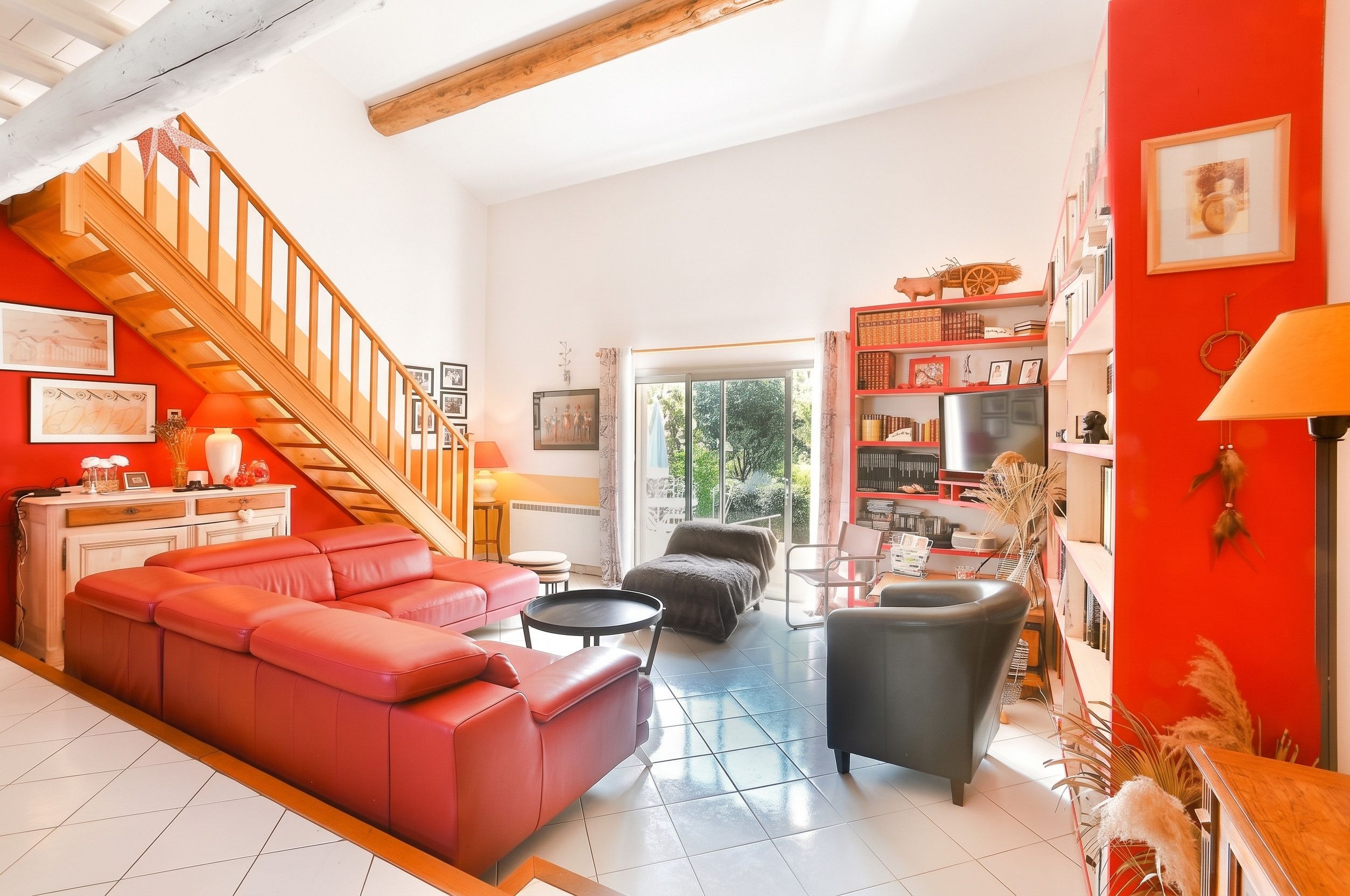 A spacious living area with a red sofa, a black armchair, and a wooden staircase.
