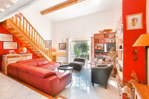 A spacious living area with a red sofa, a black armchair, and a wooden staircase. - Homerez - Enchanting Villa with Private Pool in Eyragues (Eyragues)