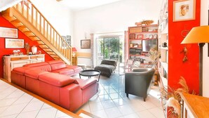 Un amplio salón con un sofá rojo, un sillón negro y una escalera que sube a un piso superior.