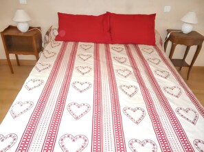 Un lit recouvert d’une couvre-lit à motifs rouges et blancs, deux tables de chevet avec des lampes et un plancher en bois.