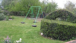 A green swing set in a well-maintained garden with a hedge and a small shed in the background. - Homerez - House in Bernac-Dessus (Bernac-Dessus)