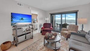 A living room with a TV, sofas, a coffee table, and a view of the outdoors. - Beachfront 2B/2B Vacation Condo At Carlos Pointe Resort With Amazing Views! World Famous Sunsets! Southern Tip of Island! (Fort Myers Beach)