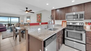 A modern kitchen with granite countertops, stainless steel appliances, and a dining area with a red accent wall. - Beachfront 2B/2B Vacation Condo At Carlos Pointe Resort With Amazing Views! World Famous Sunsets! Southern Tip of Island! (Fort Myers Beach)