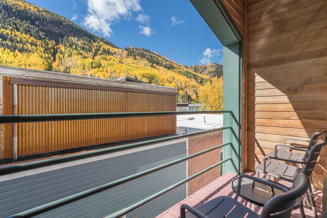 A balcony with a view of a forested mountain, metal chairs, and a wooden railing.