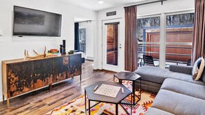A modern living room with a large flat-screen TV, a rustic wooden cabinet, a grey sofa, and a patterned rug. - Can't Beat Location! Enjoy the Balcony, Close to Gondola & Town Park (Telluride)