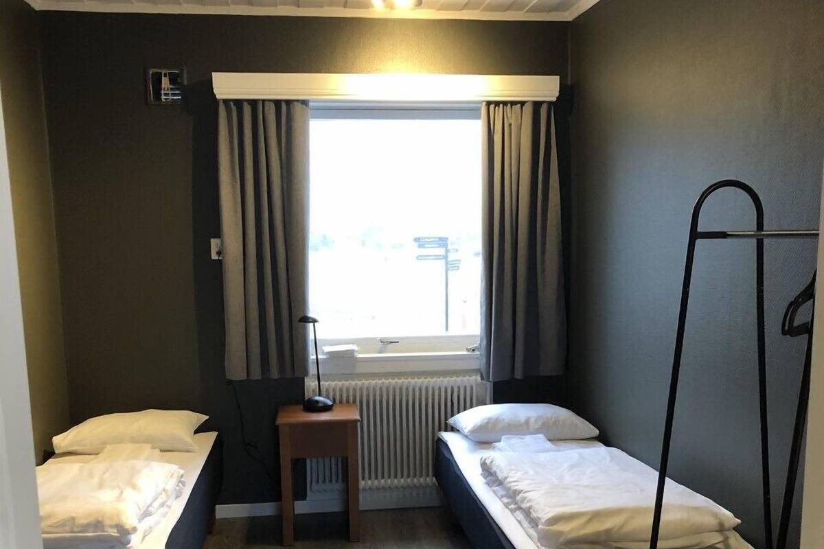 Une petite pièce bien éclairée, avec deux lits simples, une petite table et un radiateur.