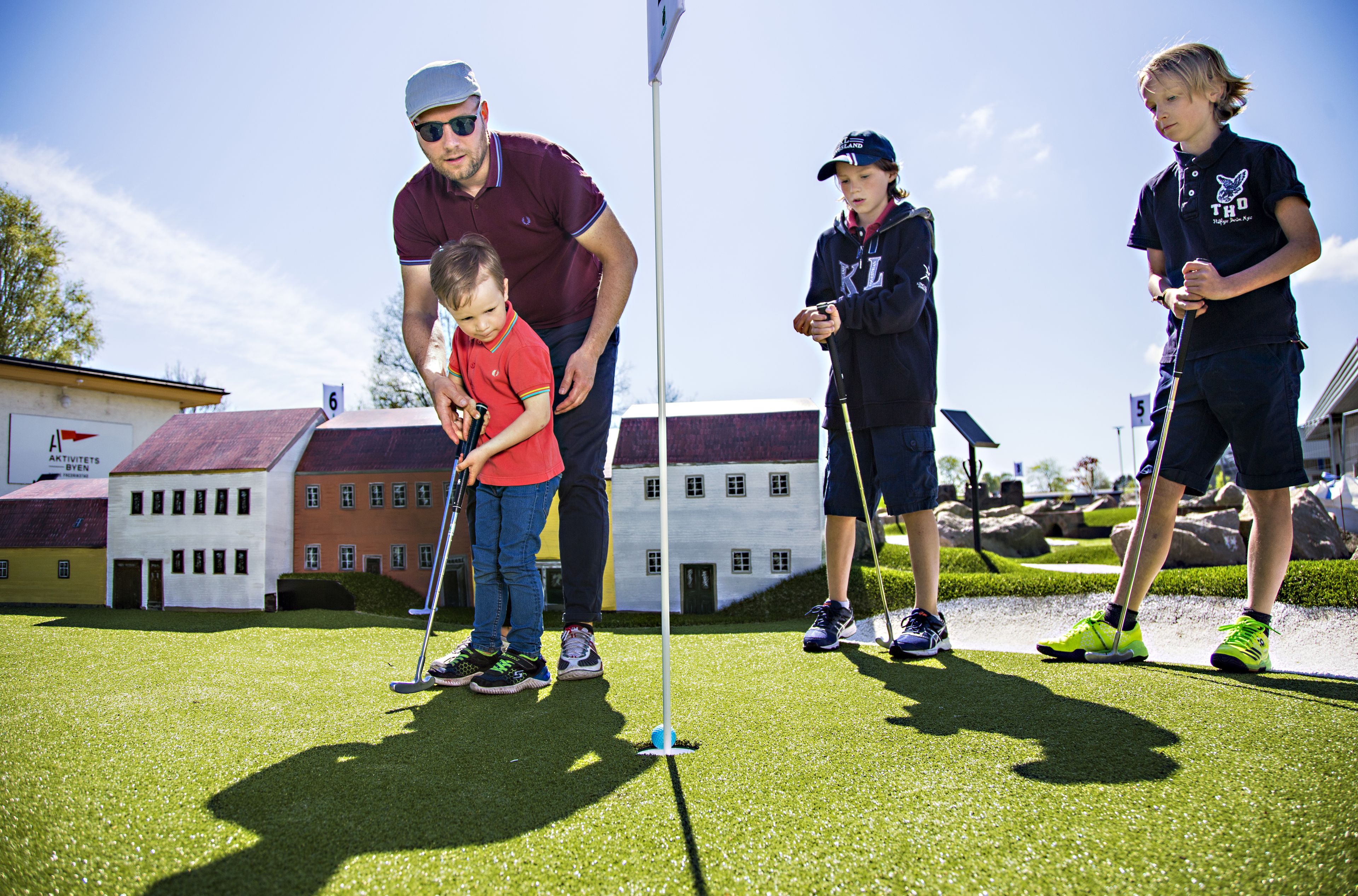 Un grupo de personas jugando al golf en un campo verde con edificios al fondo.