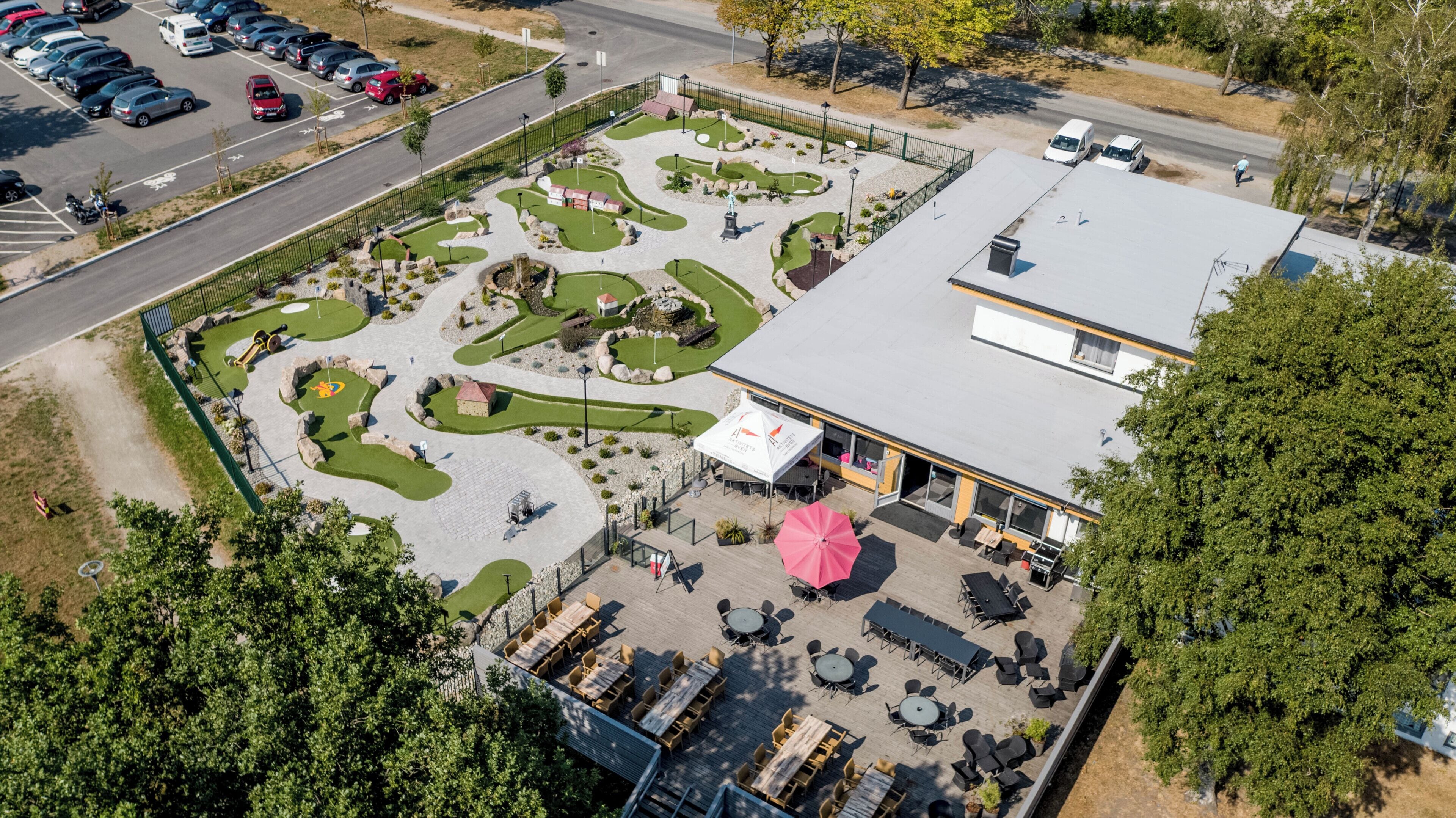 An aerial view of a golf course with a building adjacent to it, featuring a patio area with tables and chairs.