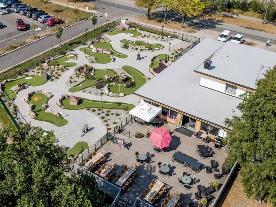 An aerial view of a golf course with a building adjacent to it, featuring a patio area with tables and chairs.