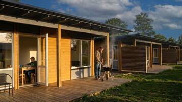 Un espacio exterior moderno con terraza de madera, una parrilla y una mesa de comedor con sillas.
