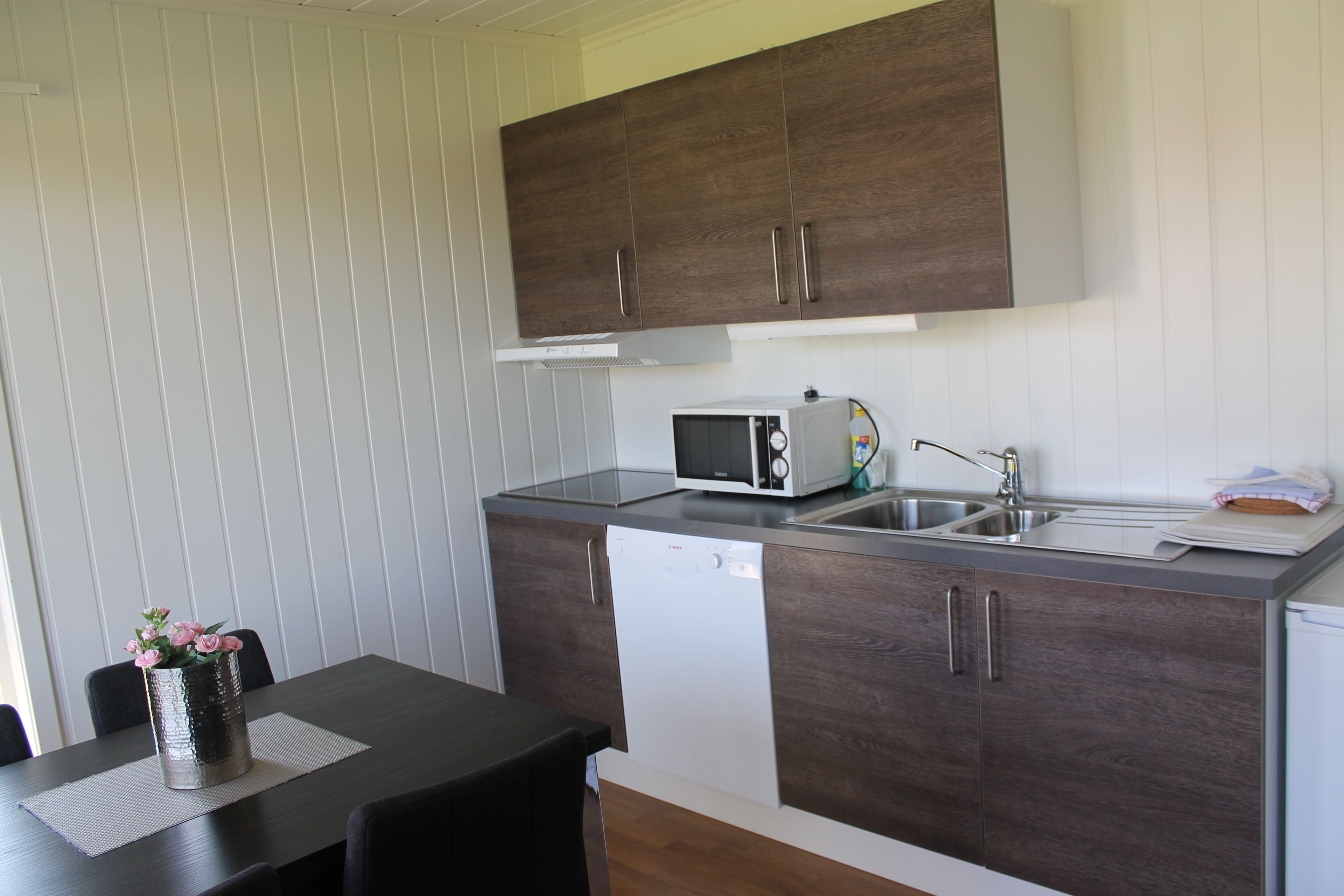 A compact kitchen with dark wood cabinets, a white dishwasher, and a microwave.