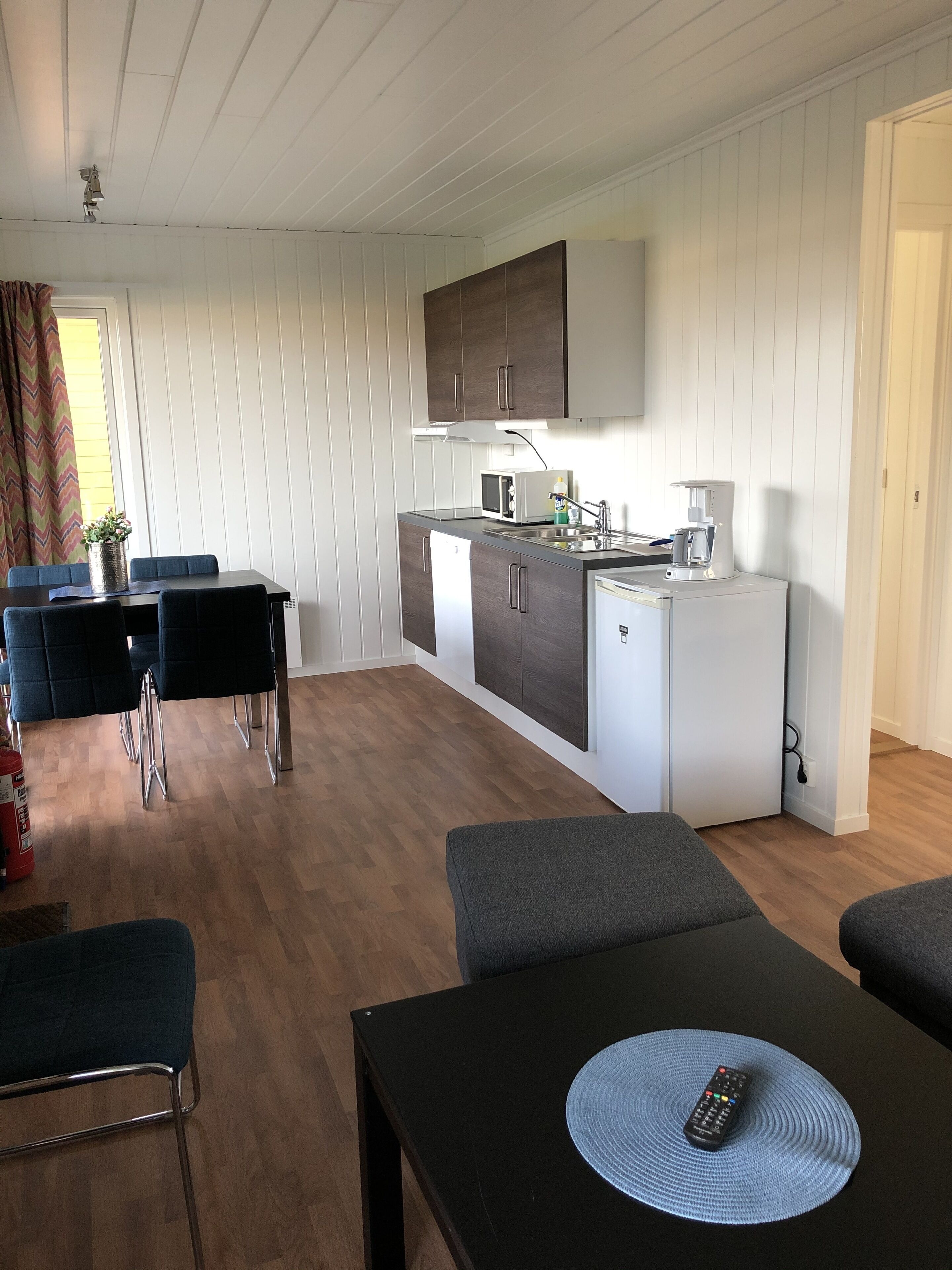 Cuina compacte amb microones, cafetera i nevera petita. Zona de menjador amb taula i cadira, i espai kitchenette amb armaris i taulella.