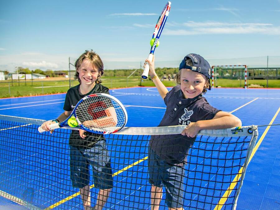 Two children playing tennis on a blue court with a net.