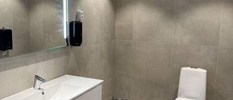 Un baño moderno con tocador blanco, un espejo grande y un inodoro.